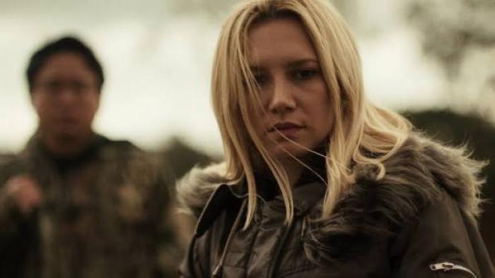 Elize: Shadows of a Woman movie: Blonde woman in a fur-trimmed jacket outdoors, with a blurred figure in the background.