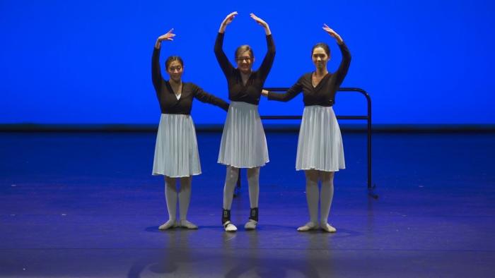 Three ballet dancers on stage with arms raised against a deep blue background.