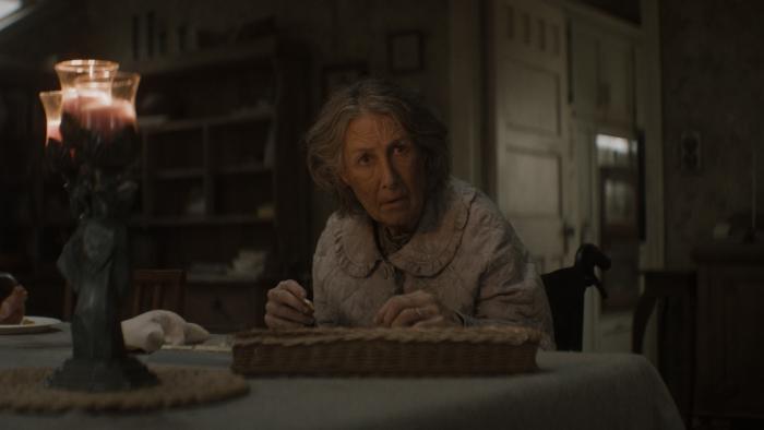 Evil Dead Burn Movie: Grandma Polly (Maude Davey) looks up from her seat at the table, a strange candle burning nearby