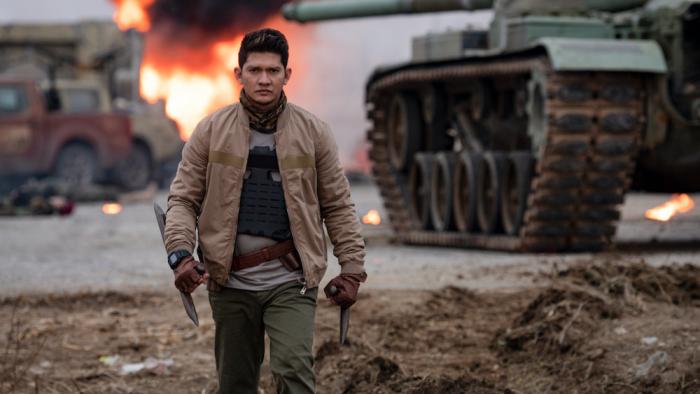 Expend4bles Movie: Villain Rahmat (Iko Uwais) walks through a battle scene, holding two bladed weapons