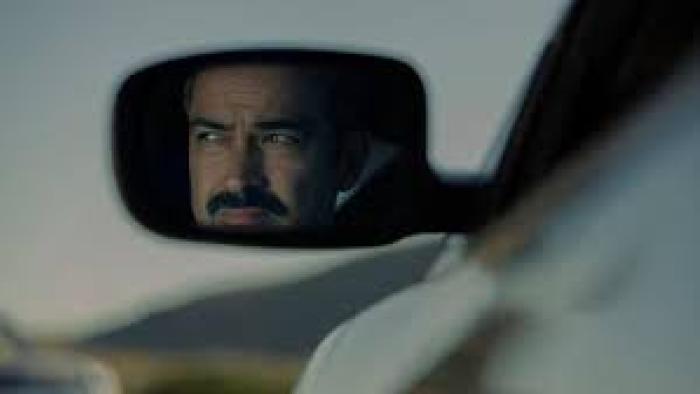 Facing El Chapo movie: Man's reflection in car side mirror against blurred landscape.