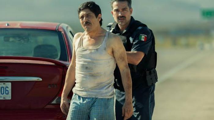 Facing El Chapo movie: Man arrested by officer beside red car on desert road.