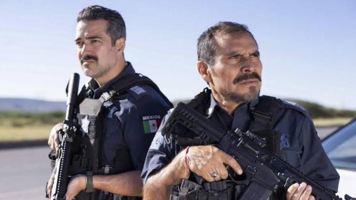 Facing El Chapo movie: Two police officers with rifles stand outdoors under a clear sky.