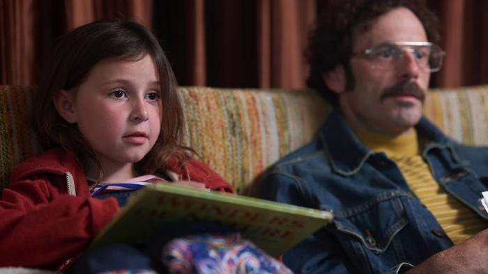Fairyland Movie: Young Alysia, holding a children's book, sits on the couch next to her father, as if watching television