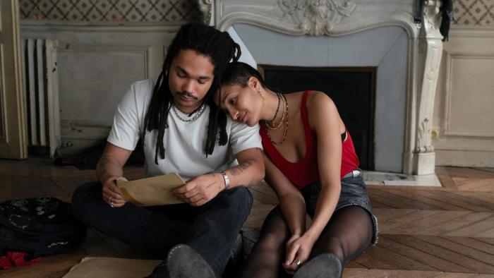 Father Mother Sister Brother movie: Two twins—an adult man and woman—sit on a wooden floor reading a document together in front of an ornate fireplace