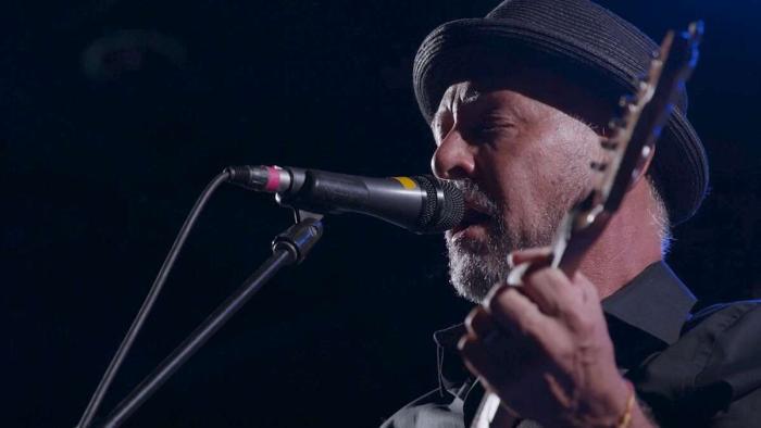 A Father's Promise Movie: Present-day Mark Barden, wearing a hat, eyes closed, sings passionately into a microphone and plays guitar