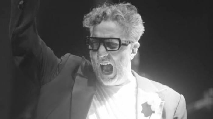 Fito Páez in a suit and glasses passionately gesturing with his arm raised.