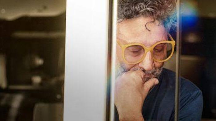 Fito Páez in yellow glasses thinking, seen through reflective glass.
