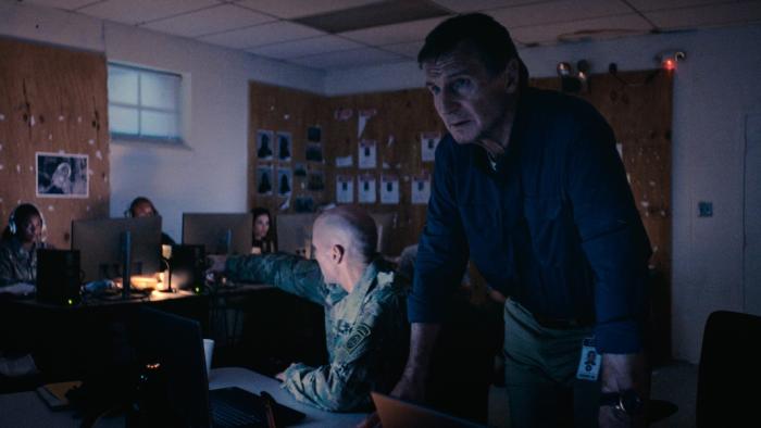 The Fix Movie: In some kind of command center, Larry (Liam Neeson) leans on a desk, his face lit by a laptop
