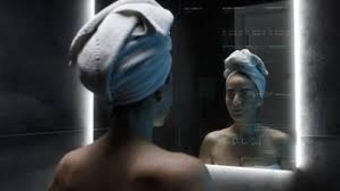 Forever Young Movie: Woman with towel on head, looking at reflection in dimly lit bathroom mirror.