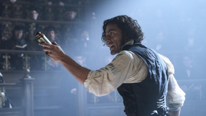 Frankenstein Movie: Holding a battery and gesturing at a crowd of scholars, Victor (Oscar Isaac) gives a furious lecture