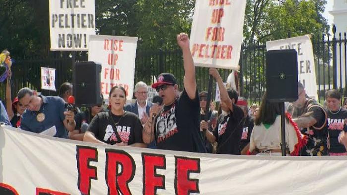 Free Leonard Peltier Movie: Protesters hold signs and a banner outdoors.
