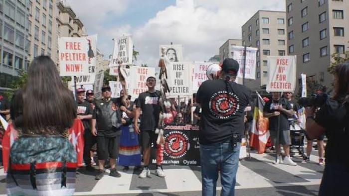 Free Leonard Peltier Movie: Crowd of activists marching with signs on a city street.