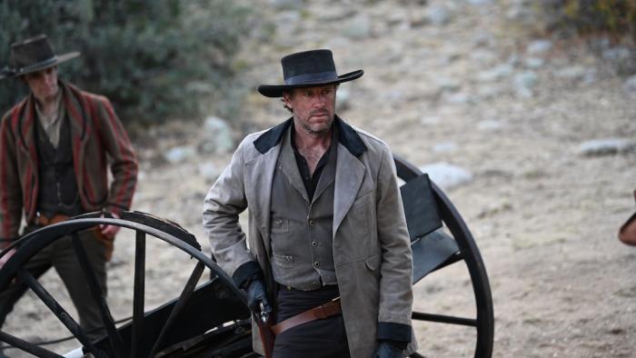 Frontier Crucible Movie: Next to the wheels of a broken coach, Edmund (Armie Hammer) reaches for his gun