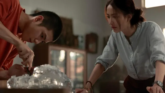 Frozen Hot Boys movie: Thai older teen boy in red t-shirt left picks at a mound of ice while Thai woman in light blue shirt right looks on