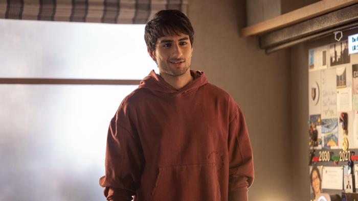 Nadaaniyan: A young Indian man with dark hair and light stubble wears a faded red hoodie, standing in a warmly lit room