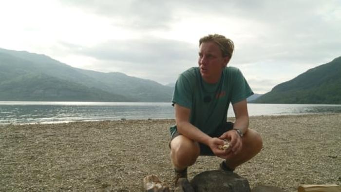 George Ezra -- End to End: George Ezra crouching on a pebble beach with mountains, sea, and sky in the background
