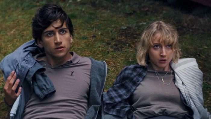 Get Away: Sebastian Croft and Maisie Ayres lean back on grass together, looking at someone standing out of shot