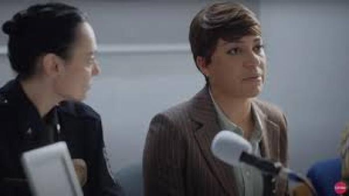 Girl in the Video movie: Two people seated at a table with microphones, one in a suit, the other in a uniform.