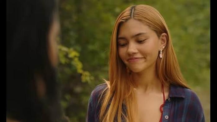 Girls Like Girls movie: A woman with long hair smiles outdoors, with blurred greenery in the background.