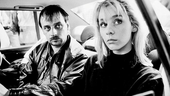 Black and white photo of a man and woman in a car, both look very haggard.
