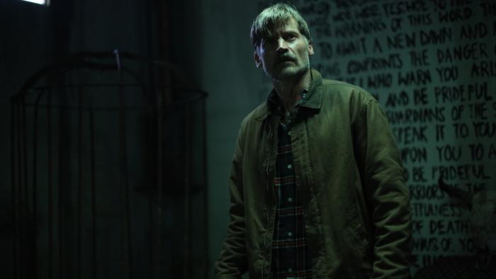 God Is a Bullet Movie: Bob Hightower (Nikolaj Coster-Waldau) explores a dark basement that has some kind of scripture written on the wall behind him