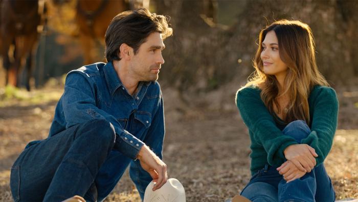 God's Country Song: A man and a woman sit outside in a field looking longingly at eachother