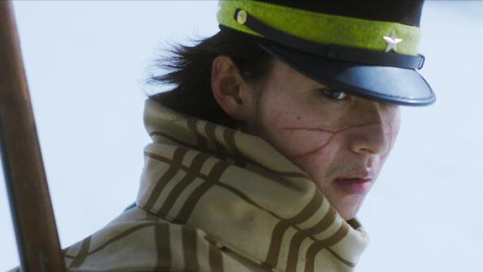 Golden Kamuy movie: Japanese soldier with scarf, soldier cap, gun on back, and face scars looks serious