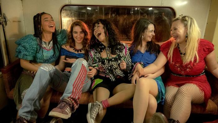 Greatest Days: Five teenage girls sit on the back seat of a bus, smiling and laughing