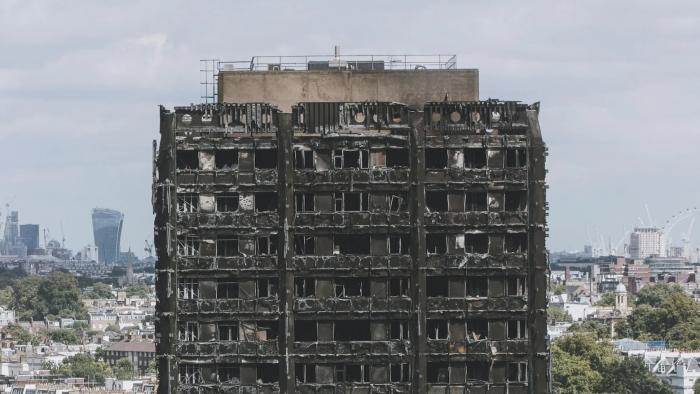 Grenfell—Uncovered: The top few floors of the burned Grenfell Tower are shown against a city backdrop