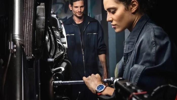 GTMax movie: French woman and French man in black mechanic jumpsuits right and center work on motorcycle left