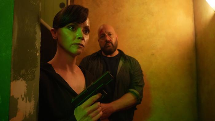 Guns Up movie: Christina Ricci holds a gun with Kevin James standing behind her in a dark hallway