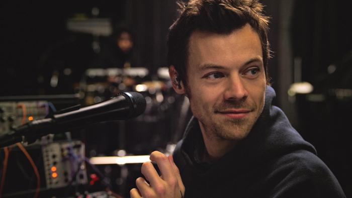 Harry Styles — One Night in Manchester: Harry Styles stands behind a tech desk with a microphone pointed toward him
