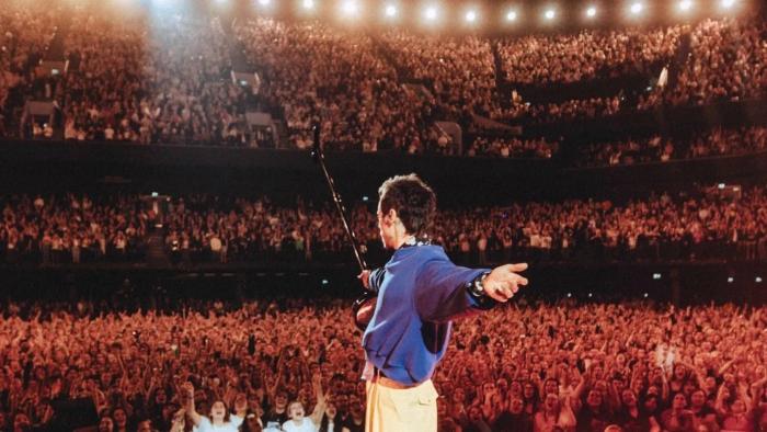 Harry Styles — One Night in Manchester: Harry Styles stands onstage with his arms stretched out to either side as he looks out into the crowd