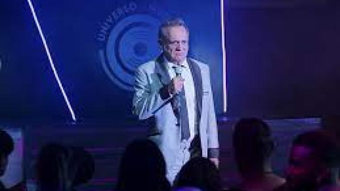 Have a Nice Day: Mexican man in white suit stands with microphone in front of a crowd at nightclub