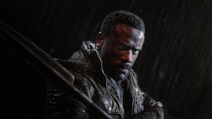 Heart of the Hunter movie: South African Black man in black jacket and spear center stands in the rain