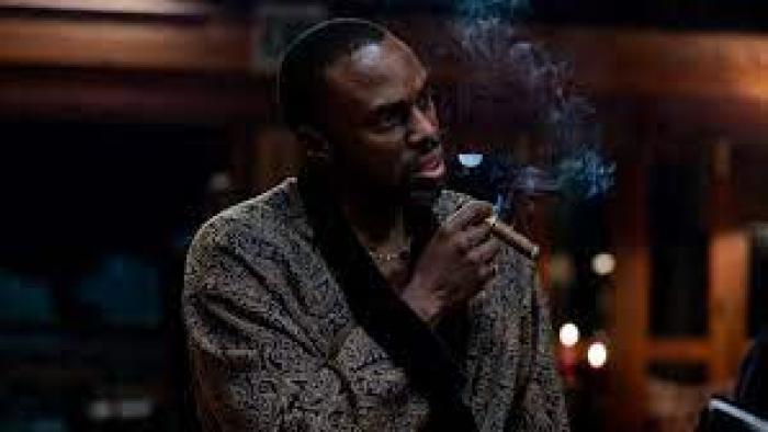 Heart of the Hunter movie: South African Black man in robe center smokes cigar