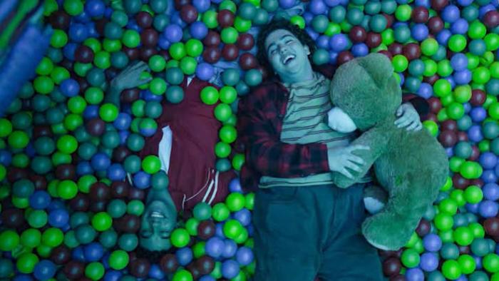 Here the Whole Time: Two people laughing in a ball pit, one holding a teddy bear.