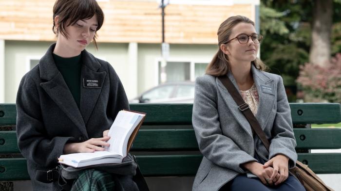 Heretic Movie: On a park bench, Sister Barnes (Sophie Thatcher) reads a book next to Sister Paxton (Chloe East)