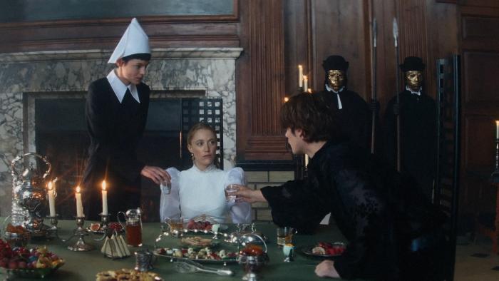 100 Nights of Hero: A young White woman sits at an imposing dinner table as her maid and a male houseguest offer her water from either side