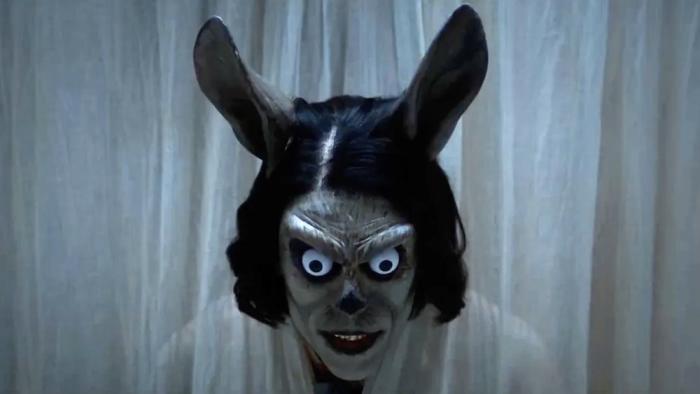 Hokum Movie: A creepy figure with bug eyes, rabbit ears, and no nose leers