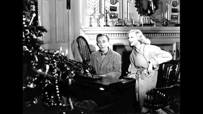 Holiday Inn Movie: A White man sits at a piano next to a White woman, both in front of a Christmas tree