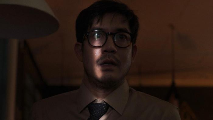Home for Rent movie: Thai man in close up wears glasses in dark living room while a sliver of light strikes his face