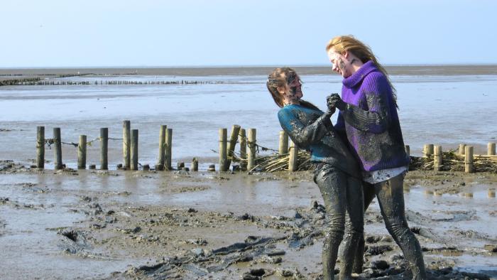 Of Girls and Horses Movie: Two people joyfully playing in a muddy beach setting.