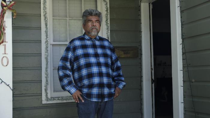 How the Gringo Stole Christmas Movie: Bennie (George Lopez) stands on his front porch, which is decorated for Christmas, looking grumpy