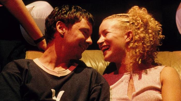 Human Traffic: A young White man and woman smiling at each other on a couch in a nightclub