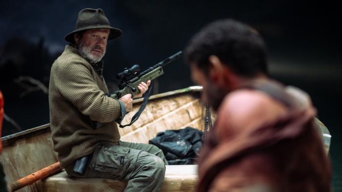 Hungry Movie: On a boat, Walker (Joaquim de Almeida) points his tranq gun and looks back at the wounded Rodrigo