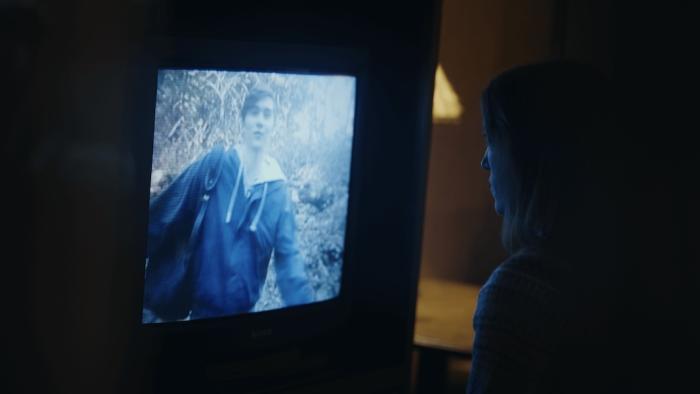 Hunting Matthew Nichols Movie: Tara, seen in profile, sits close to a TV and watches an old video of her brother