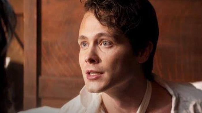 I Heard the Bells movie: Young man with curly hair speaking, indoors, with warm lighting.
