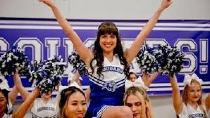 Identity Theft of a Cheerleader: Cheerleader lifted by teammates, smiling with arms raised, in front of "Cougars" banner.